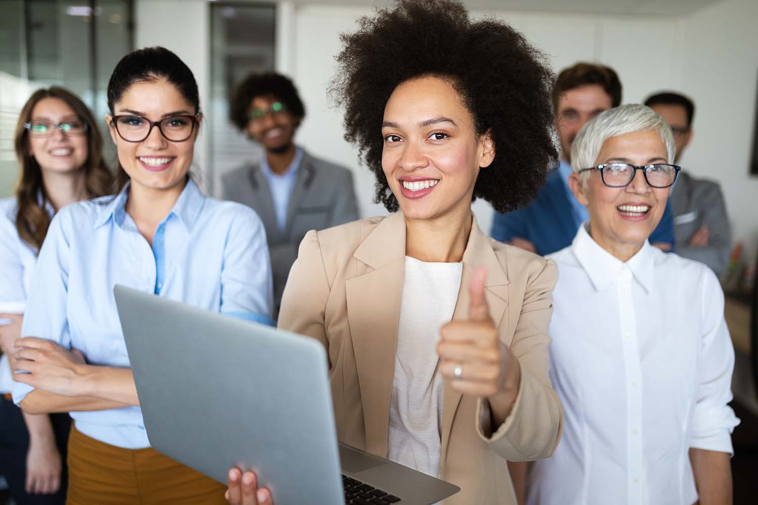 A smiling team of colleagues, one giving a thumbs up while holding a laptop.