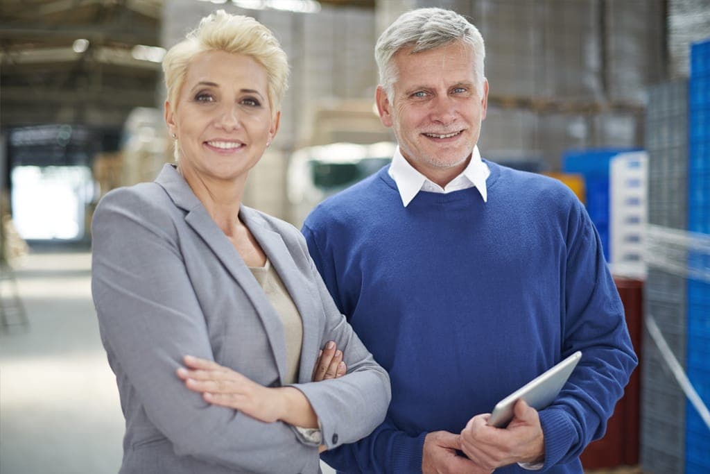 Two business owners standing together in a warehouse, one holding a tablet.