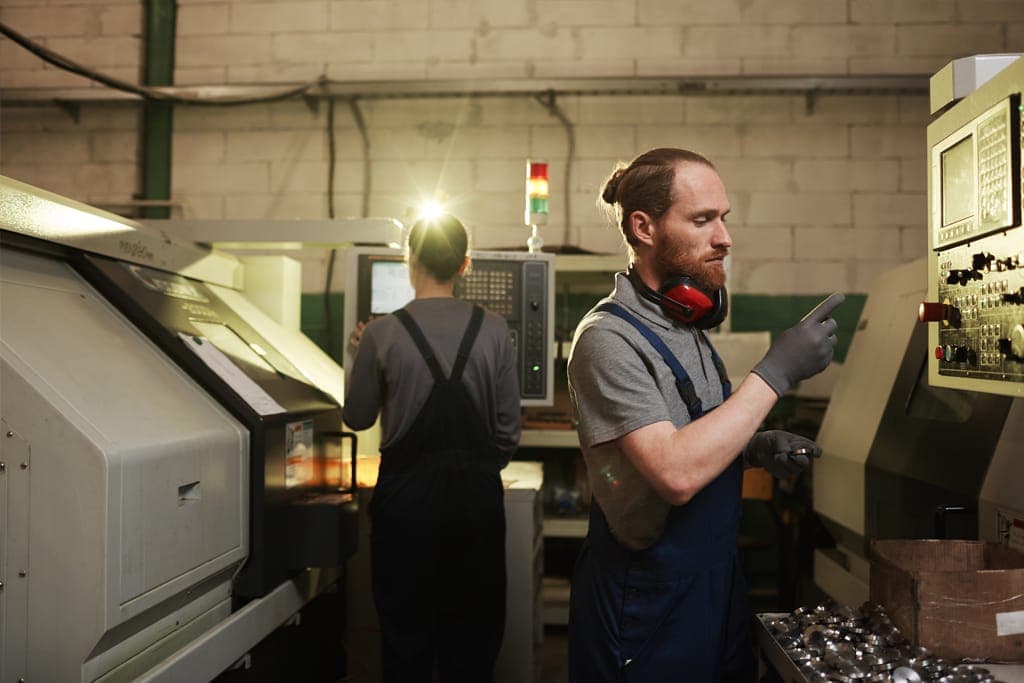 Two machinists operating CNC lathes on a small manufacturing shop floor.